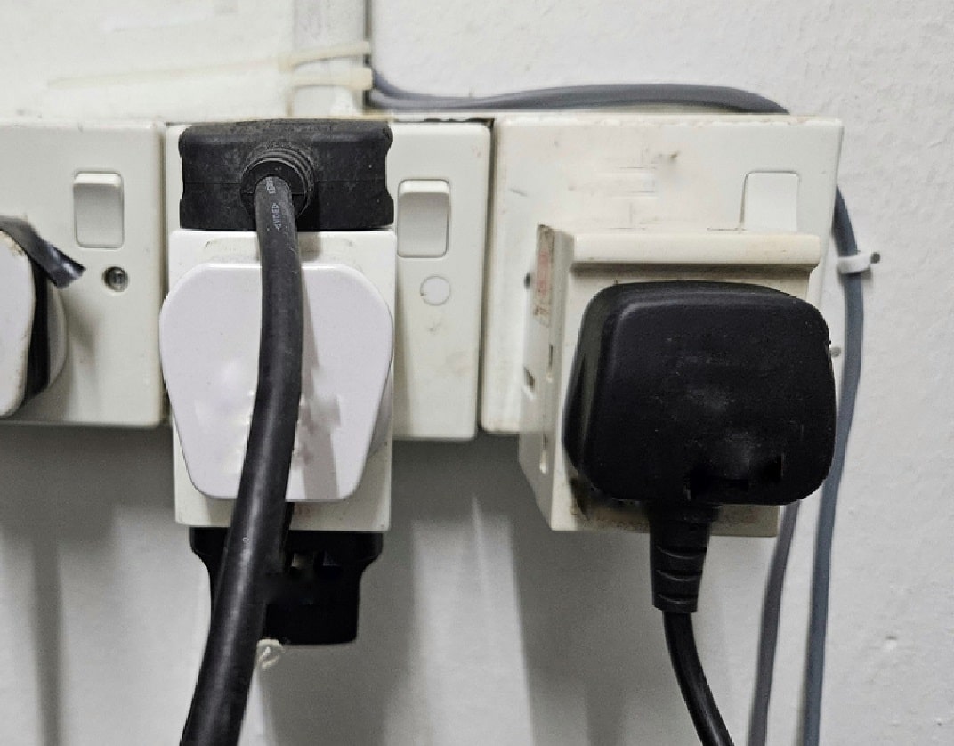 two white plastic adapter blocks plugged into two single socket outlets, one with three plugs plugged into the black the other with one