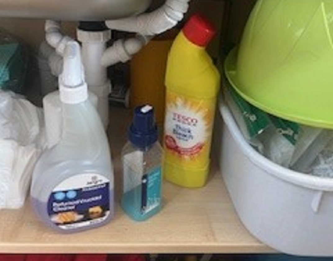 close-up of under-sink cupboard with various bottled substances including bleach