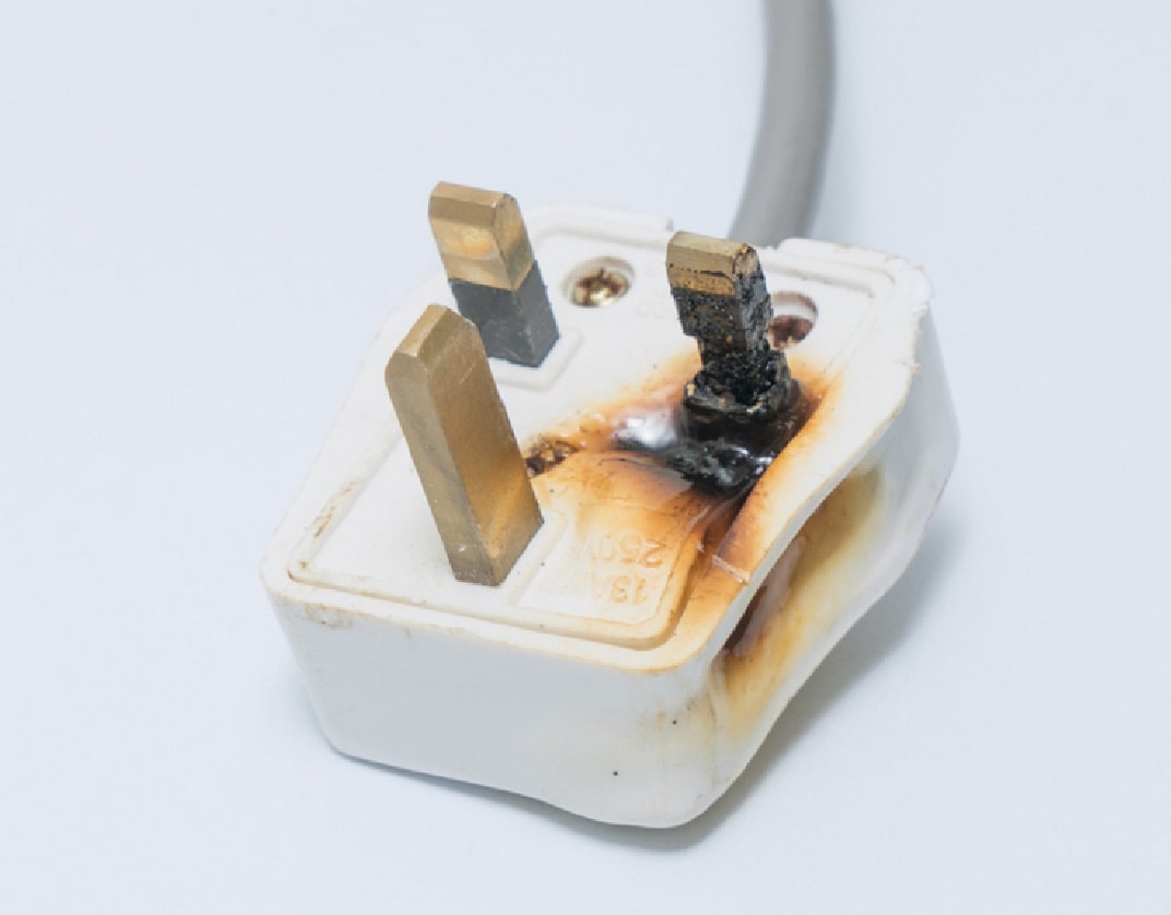 close-up of white plastic UK plug with burning marks around one of the conductor pins