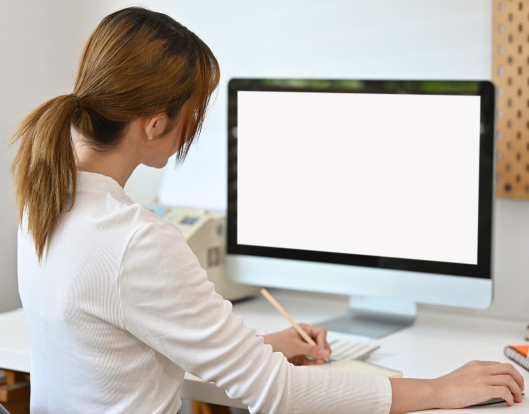 lady sitting in front of display screen at an angle to desk and has her mouse far to right, which could lead to shoulder problems