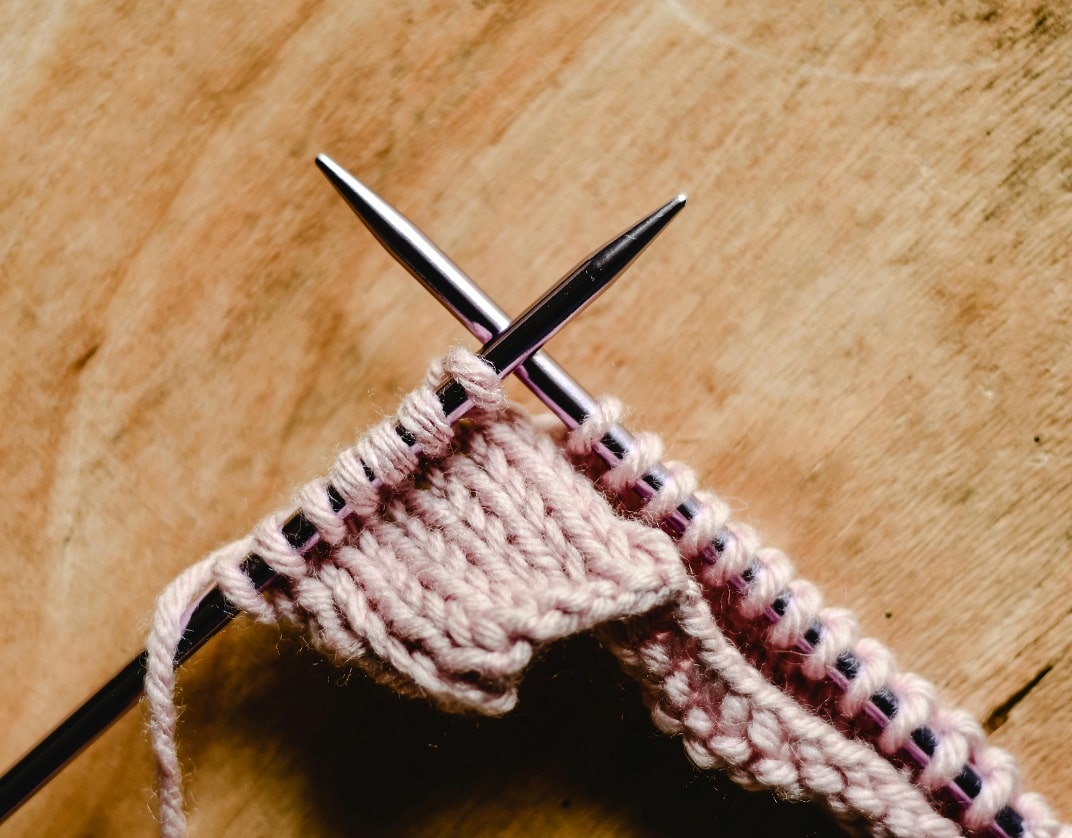 close-up of a pair of knitting needles and a few rows of light pink knitting