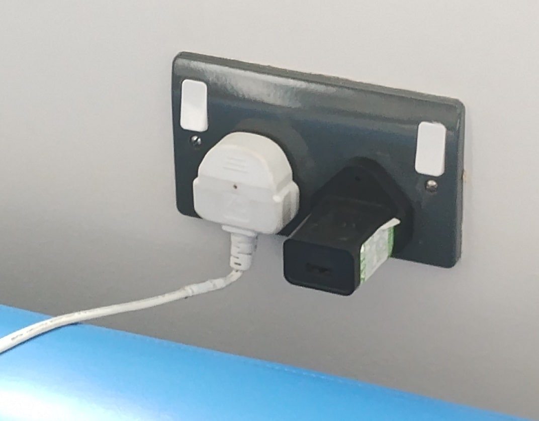 moulded white plug in wall outlet with flex bent at 90 degrees due to promimity of chair under socket outlet