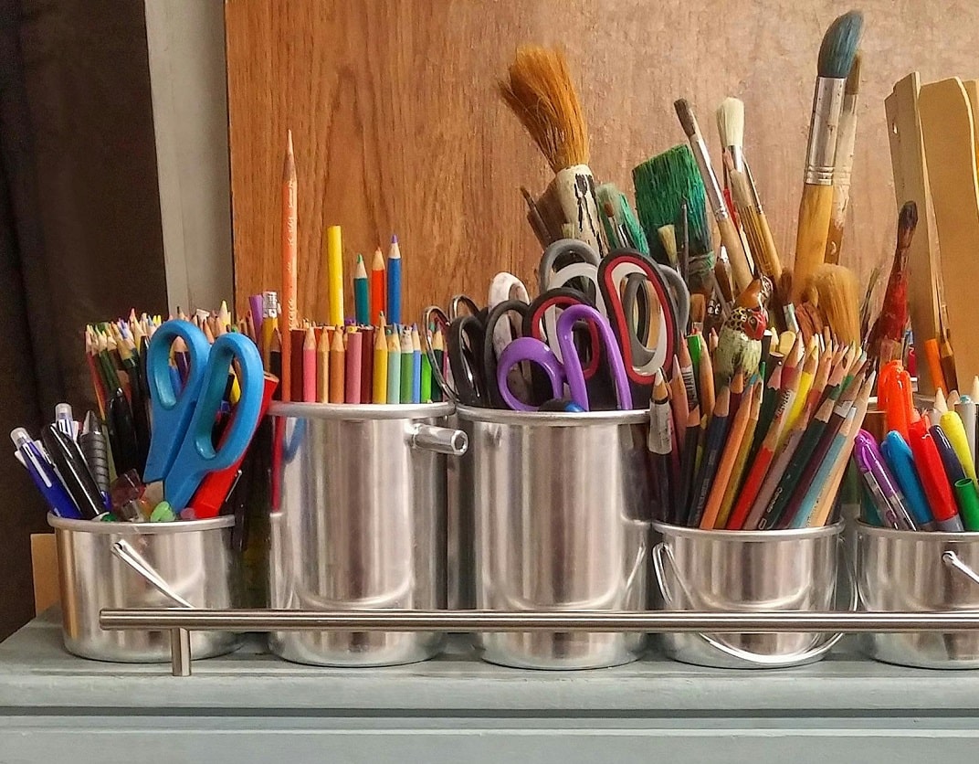 close-up of storage shelf with metal pots containing various craft items including scissors