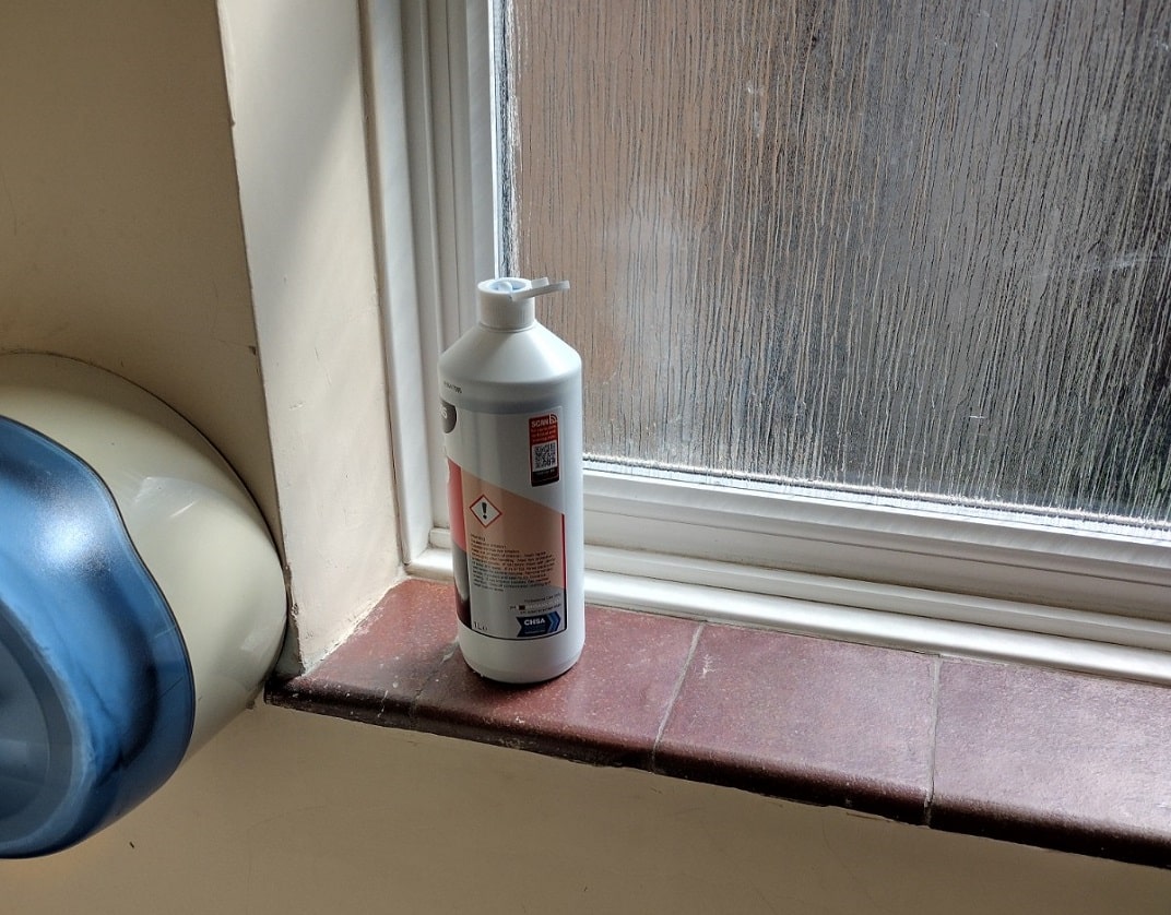 toilet cleaner bottle stood on red tiled window sill in toilet
