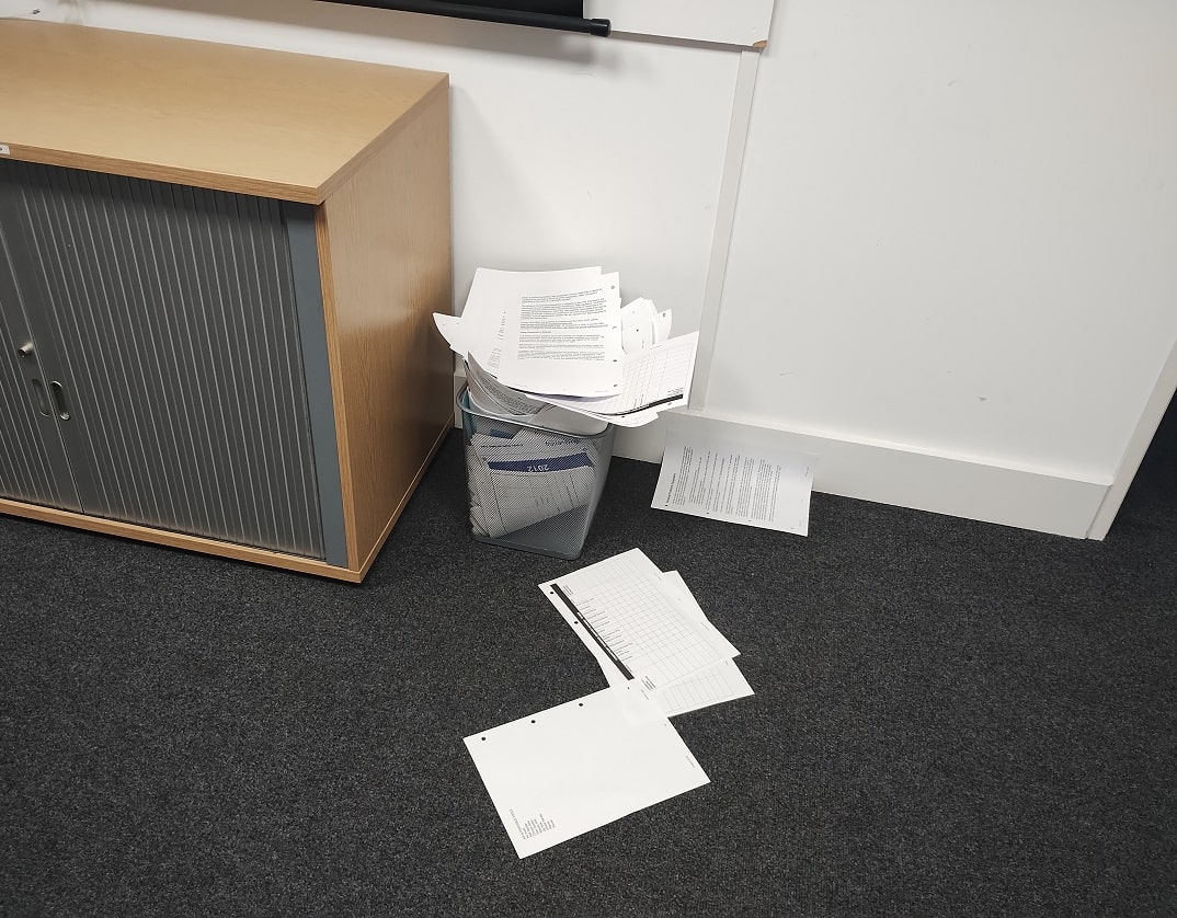 overfilled waste bin, with sheets of paper scattered across the carpet